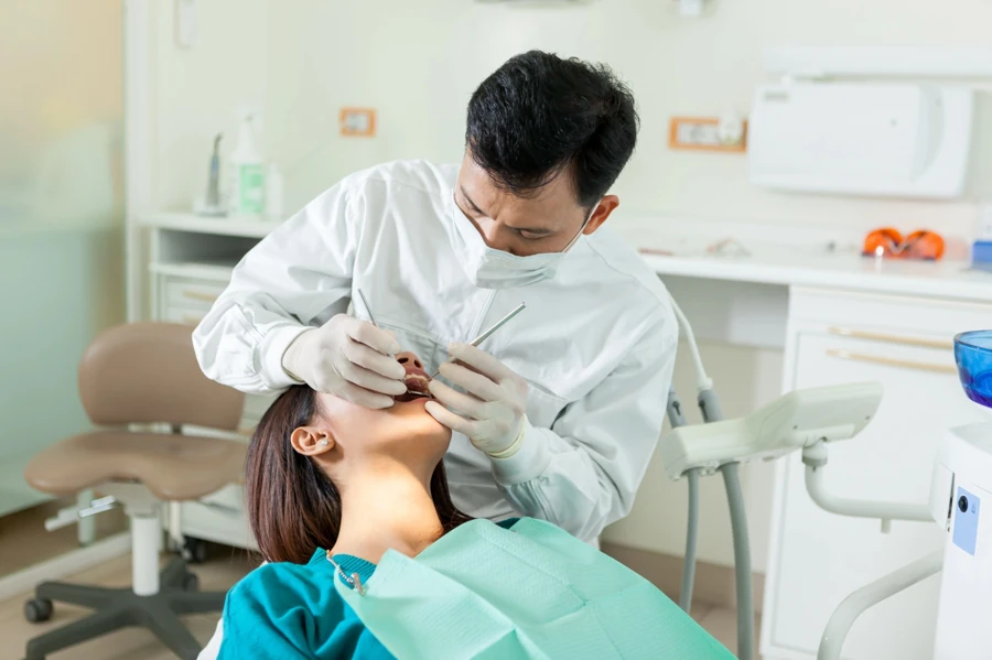 Dentist-wearing-a-mask-examining-a-patient’s-teeth-with-dental-instruments-in-a-clinical-setting